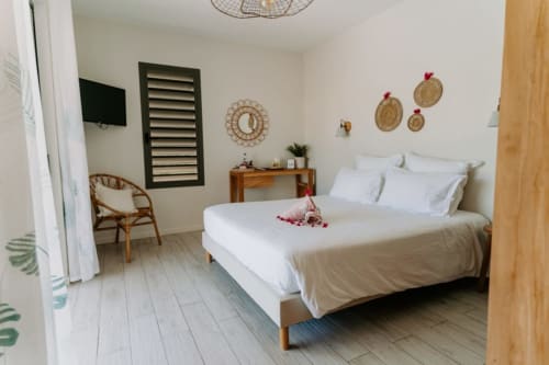 Chambre moderne à l'Habitation l'SEO à Sainte-Anne avec lit queen-size, fauteuil en rotin, bureau en bois et détails muraux décératifs