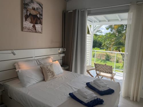 Chambre lumineuse au Domaine de la Glacière avec lit blanc, balcon vue jardin, paysage tropical, bungalow Balisier