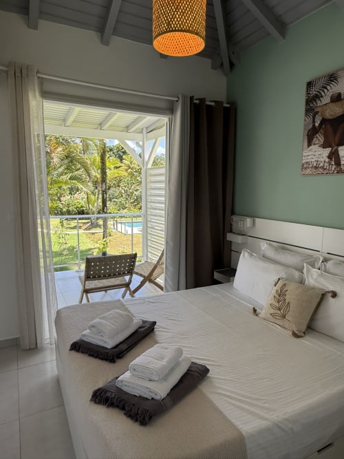 Chambre du Bungalow Alpinia au Domaine de la Glacière avec vue sur piscine, jardin tropical et balcon couvert à Petit Bourg