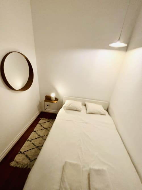 Minimalist bedroom at Royal Prince Garden Apartments in Lisbon with white bed, round mirror, pendant lamp, and patterned rug.