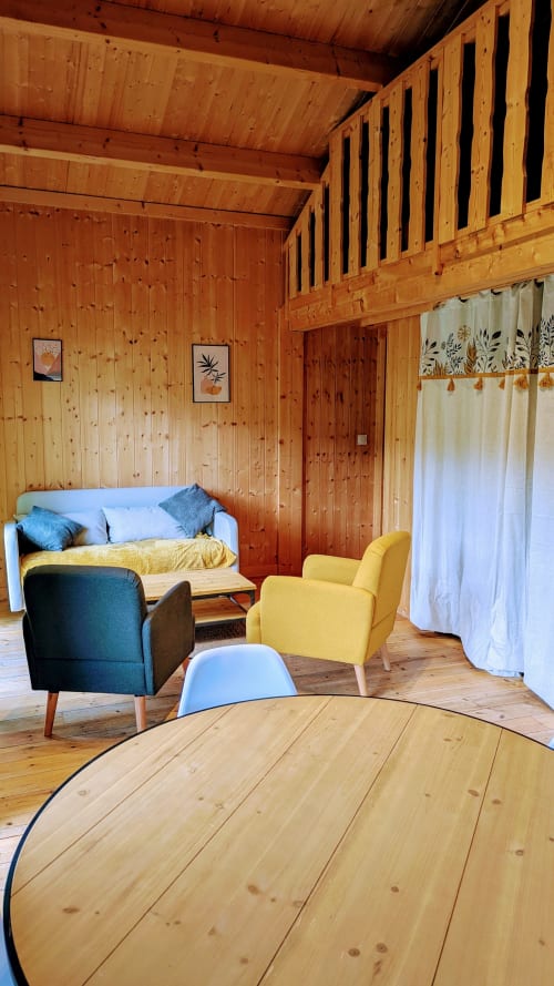 Interno moderno di lodge in legno con divano, poltrone e letto alle Cabanes du Belvédère, Serrières-sur-Ain