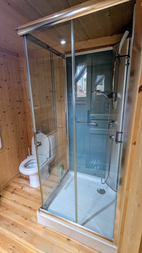 Moderna cabina doccia in vetro nel bagno di una lodge in legno con toilette e luce naturale dalle finestre