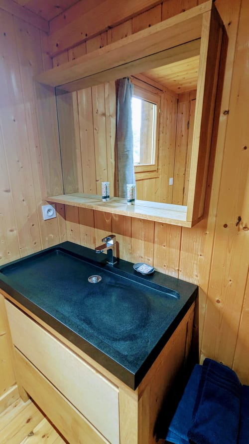 Bagno moderno con lavabo in pietra scura, specchio grande e pareti in legno nel lodge La Cormière di Cabanes et lodges du Belvédère