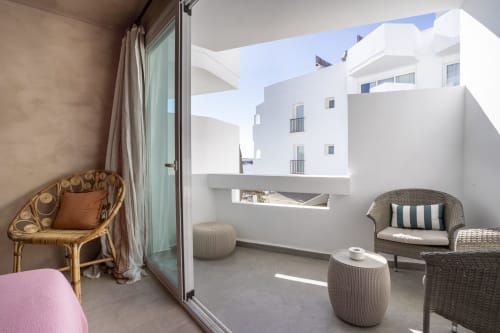 Balcón del estudio Formentera Especial Luna con sillas de mimbre, cojines rayados y vistas a edificios blancos de La