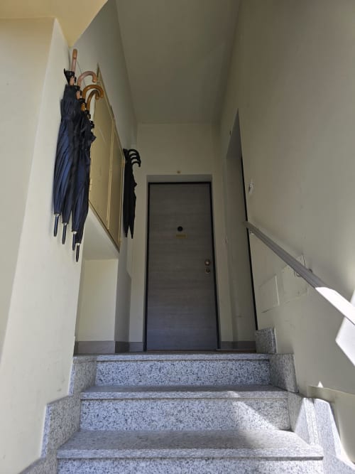 Stepenice u apartmanu Raymihome u Torinu s kišobranima obješenim na zidu i tamnim vratima na vrhu