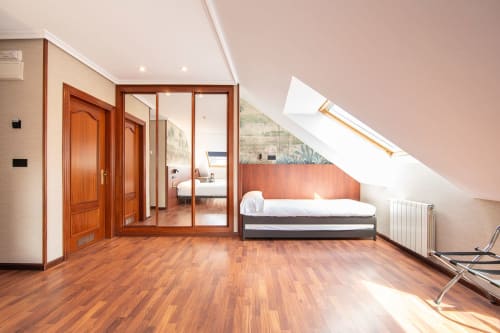 Espacioso dormitorio abuhardillado en Hotel Puerto De Candás con suelos de madera, cama individual, armario espejo, claraboya y vistas al mar