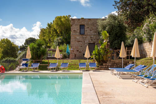 CefalHome pool with turquoise water, sun loungers, stone building, and lush gardens under blue sky