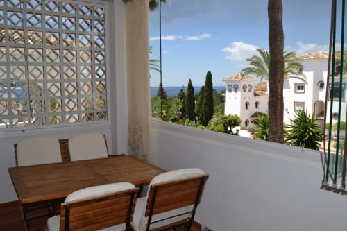 Balcón de apartamento en Marbella con mesa de comedor, vista al mar, decoración blanca y arquitectura mediterránea