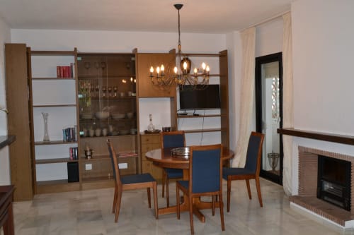 Comedor moderno del apartamento SACORO en Marbella con muebles de madera, sillas azules, lámpara de araña y vistas al mar