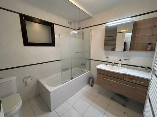 Baño moderno en apartamento SACORO en Marbella con azulejos blancos, tocador de madera, ducha acristalada y bañera