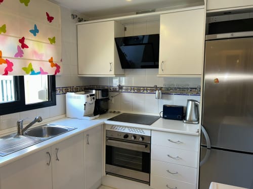 Cocina moderna blanca en apartamento SACORO, Marbella, con electrodomésticos de acero inoxidable y decoración de mariposas coloridas en la pared