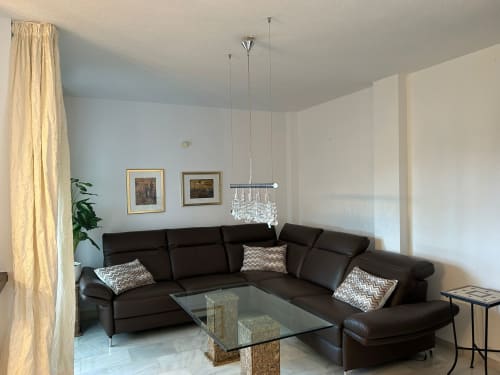 Elegante sala de estar moderna en SACORO Marbella con sofá seccional negro, araña de cristal y vistas al mar