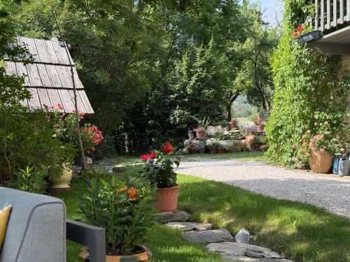 Charmante cour fleurie des Méans B&B à Meolans-Revel avec pergola couverte de lierre, plantes en fleurs et allées de gravier.