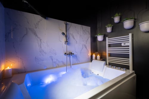 Luxury bathroom with illuminated marble shower wall, blue-lit Jacuzzi tub, and heated towel rack at Wellkhome Bordeaux
