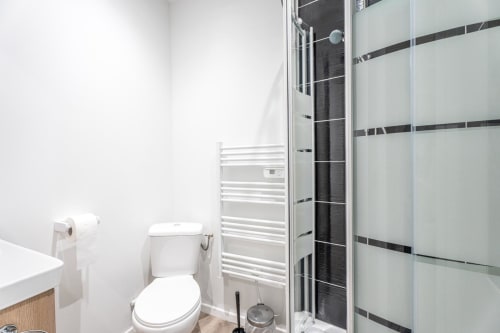 Modern bathroom in Wellkhome apartment, Bordeaux featuring white toilet, heated towel rail, frosted glass shower enclosure