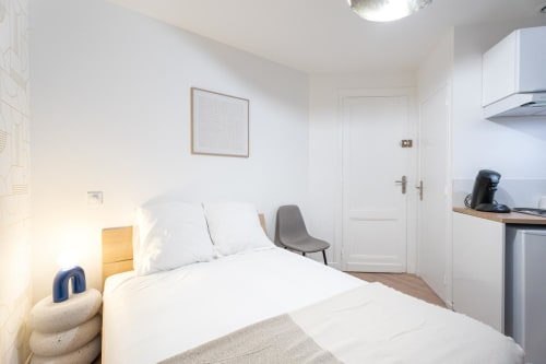 Modern studio apartment bedroom in Bordeaux with white bedding, kitchenette, and city view at Wellkhome Appartements