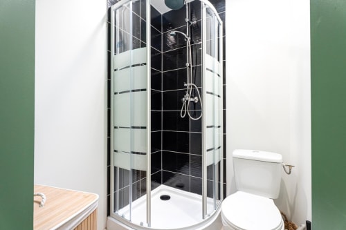 Modern shower cubicle with black tile walls in Wellkhome apartment, Bordeaux, beside white toilet