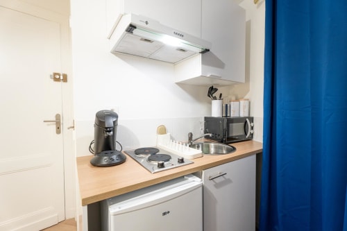 Compact kitchenette in Bordeaux apartment with cooktop, microwave, coffee maker, and wooden countertop