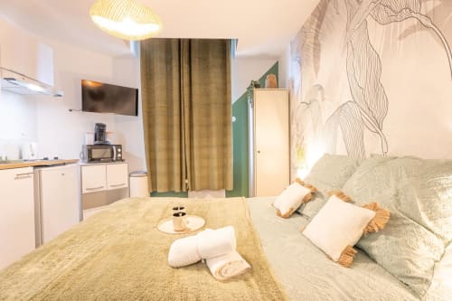Modern studio apartment bedroom at Wellkhome Bordeaux with bed, kitchenette, TV, and botanical wall art