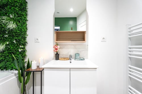 Modern bathroom at Wellkhome Bordeaux with white vanity, green accent wall, wooden mirror, and living green wall feature