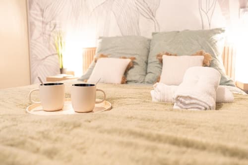Cozy bedroom at Wellkhome Appartements in Bordeaux with two coffee mugs on bed, white towels, and green pillows