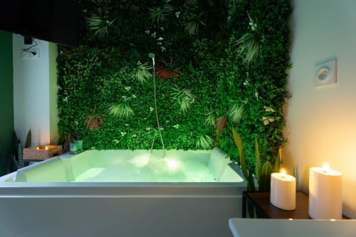 Luxurious Jacuzzi bathtub surrounded by lush living wall with tropical plants and candles, Wellkhome Bordeaux