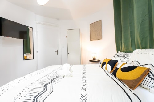 Modern studio apartment at Wellkhome Bordeaux with white bedding, green curtains, and compact living space featuring TV and