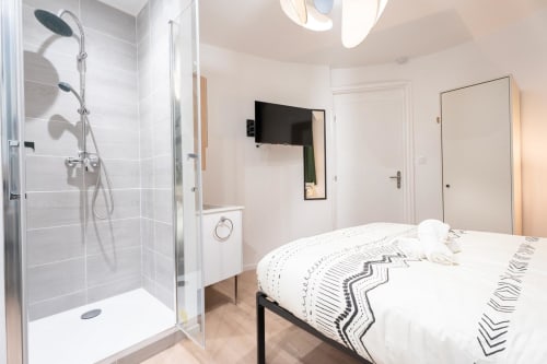 Modern studio apartment in Bordeaux with ensuite shower, bed, flat-screen TV, and bright natural lighting