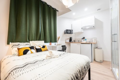 Smart Studio bedroom at Wellkhome Bordeaux with queen bed, green curtains, kitchenette, and modern amenities