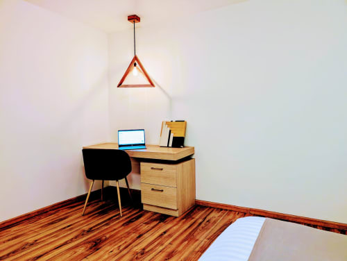 Escritorio de estudio moderno con superficie de trabajo de madera, silla negra y lámpara colgante triangular roja en Casa Donceles, Ciudad de México