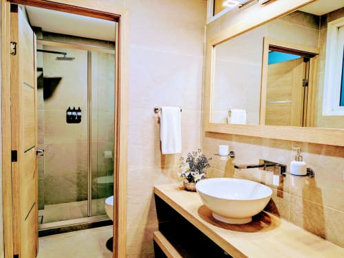 Baño moderno del hotel Casa Donceles en la Ciudad de México con lavabo de cerámica, espejo grande, mueble de madera y ducha abierta.