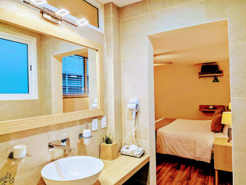 Vista del estudio Casa Donceles con baño moderno, lavabo, espejo y vista parcial de cama king con acentos naranjas