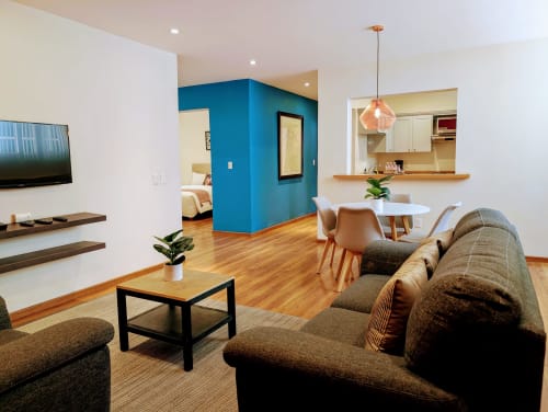 Sala de estar moderna en Casa Donceles con sofá marrón, mesa de comedor, cocina y dormitorio con pared azul destacada