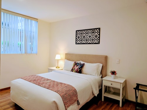 Habitación luminosa en Casa Donceles de Ciudad de México con cama queen, cabecera beige, lámpara de noche y arte de pared.