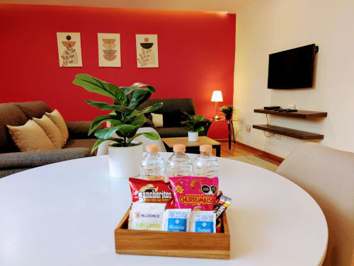 Elegante sala de estar del hotel Casa Donceles en la Ciudad de México con pared roja, sofá gris, canasta de bienvenida y planta decorativa