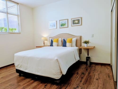 Dormitorio luminoso en Casa Donceles, Ciudad de México con cama blanca, cabecera beige, almohadas amarillas y azul marino, suelo de madera