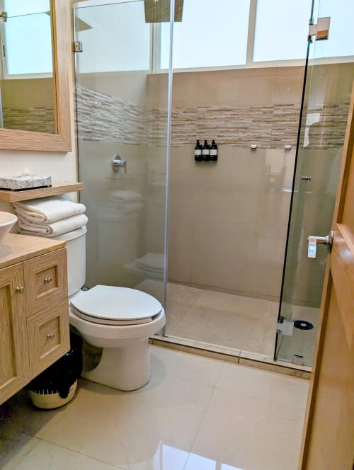 Baño moderno en Casa Donceles, México con inodoro blanco, tocador de madera y ducha con cristal y acabados de azulejo