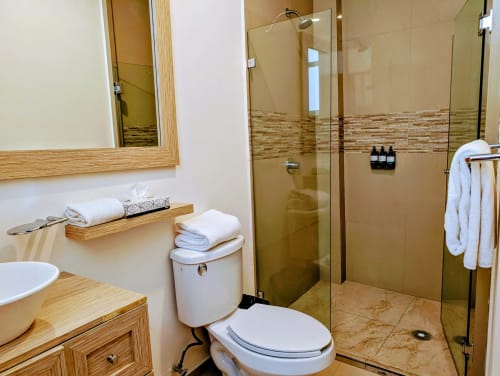 Baño moderno en el apartamento Casa Donceles de la Ciudad de México con ducha de cristal, vanidad de madera y toallas blancas