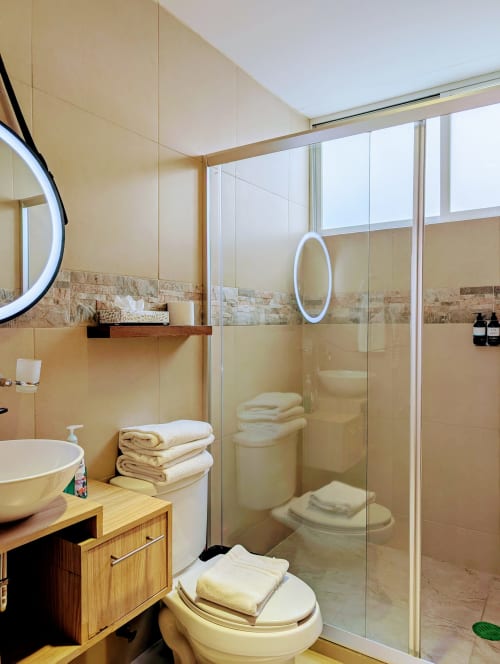 Baño moderno en Casa Donceles Ciudad de México con ducha de cristal, azulejos beige, tocador de madera y toallas blancas