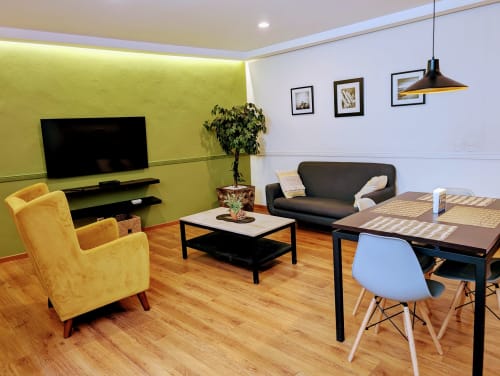 Sala de estar moderna en apartamento Casa Donceles con pared amarilla, sofá negro, sillón amarillo, mesa de comedor y tecnología