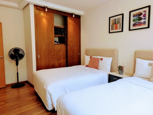 Dormitorio luminoso con camas gemelas en apartamento Casa Donceles, Ciudad de México, cabeceras beige, ropa de cama blanca, armario de madera