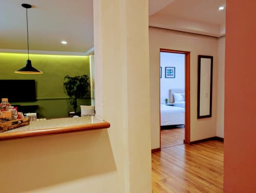 Entrada del apartamento Casa Donceles con planta abierta, pared de acento verde lima, pisos de madera y puerta roja al dormitorio