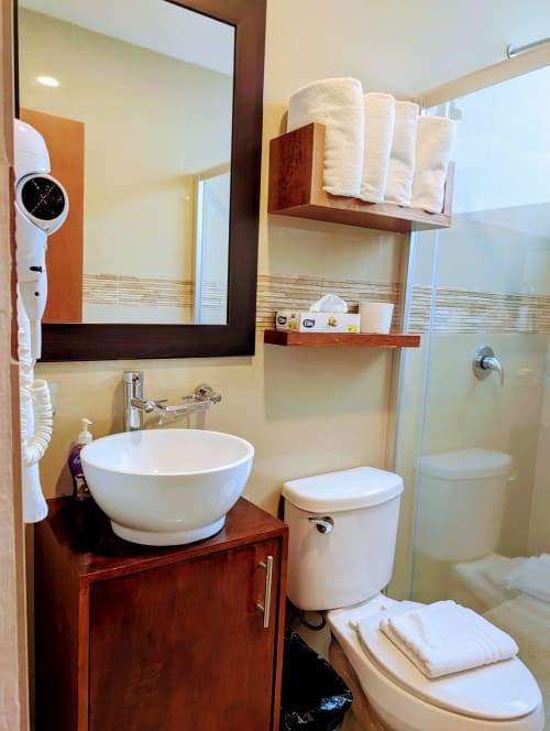 Baño moderno del hotel Casa Donceles en la Ciudad de México con lavamanos blanco redondo, inodoro, vanidad de madera y ducha de cristal