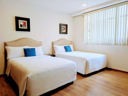 Dos camas dobles con cabeceras beige en una habitación luminosa de Casa Donceles, Ciudad de México, con sábanas blancas y detalles azules.