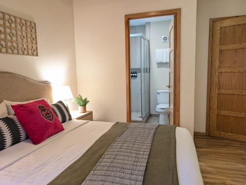 Dormitorio moderno con cama queen, almohada roja, baño privado y vistas a la ciudad en el hotel Casa Donceles Mexico City