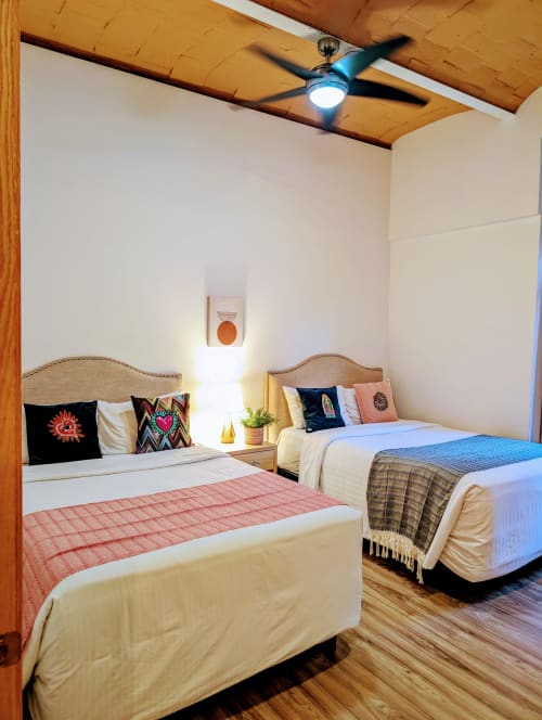 Dormitorio moderno en el penthouse Casa Donceles, Ciudad de México con dos camas, vigas de madera, ventilador de techo y almohadas coloridas