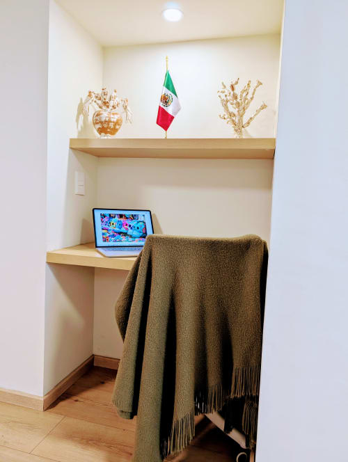 Rincón de trabajo compacto en Casa Donceles con laptop sobre escritorio de madera, bandera mexicana y manta oliva en hotel de la Ciudad de México