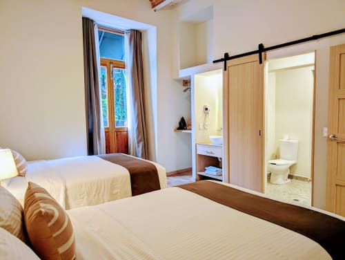Recámara moderna en penthouse Casa Donceles Ciudad de México con dos camas, baño ensuite y vistas a la ciudad por puertas corredizas