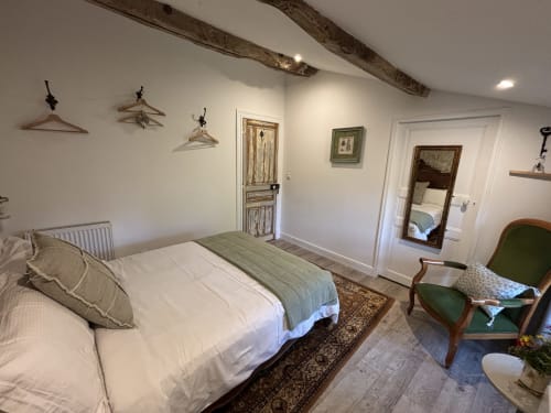 Chambre lumineuse à la Maison Mûrier à Fayssac avec literie blanche, poutres apparentes, fauteuil vert et tableaux encadrés