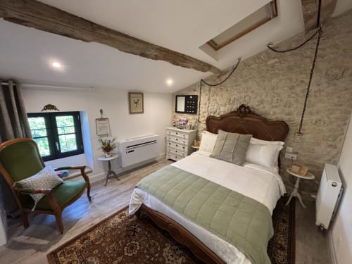 The Garden Room at Maison Mûrier B&B in Fayssac featuring a wooden bed, green chair, exposed beams, and stone walls.